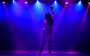 Cool singer with microphone on bright backlit stage in bright blue lights.